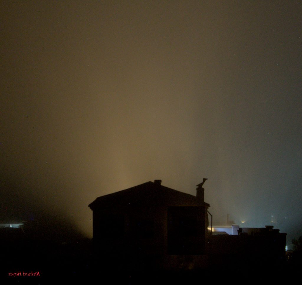 The silhouette of a house, back lit creating an orange haze around the house 